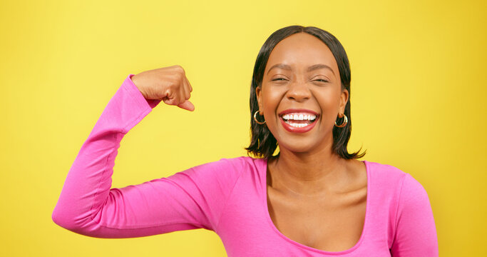 Beautiful strong woman flexes one arm, muscle, yellow studio background