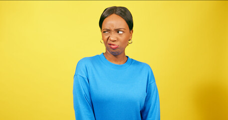 Cute young woman pulls funny face, grimace, yellow studio background