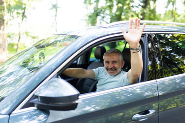 Nice middle age man greeting someone while driving