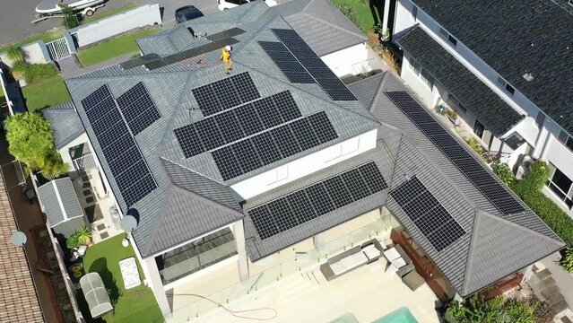 Solar panels and technician on luxury waterfront home on a sunny day.