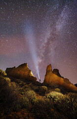 person with a flashlight near rocks with the milky way on a background © Ilia