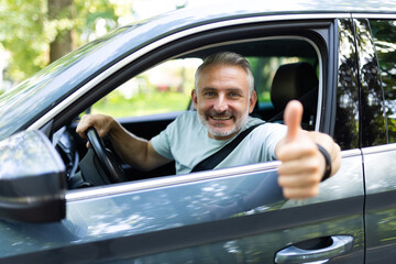 Middle age man make selfie by camera doing ok gesture while drive car at street