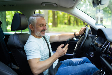 Middle aged man using a smart phone while driving a car in the street