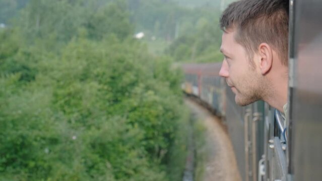 Young man looking out of train window while traveling by railway through Balkans. Male traveler looking out sleeping car window in the morning