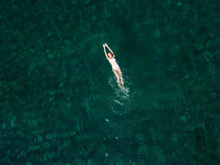 Above view of woman swimming at sea. Aerial top view of young girl in white swimsuit floating on water surface in crystal clear turquoise sea. Vacation at Paradise. Ocean relax, travel and vacation