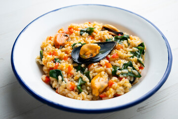 Spanish paella with mussels and spinach on white plate.