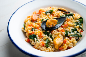 Spanish paella with mussels and spinach on white plate.