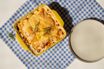 Baked potato casserole with creamy sauce and a sprig of rosemary, showcasing the flavors of French cuisine. A Gratin Dauphinois recipe featuring potatoes cooked in golden perfection, at napkin 