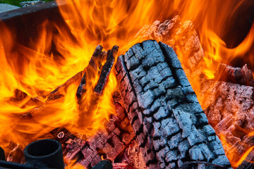 Intense flames surrounding logs inside round fire pit with exposed white ashen log close up
