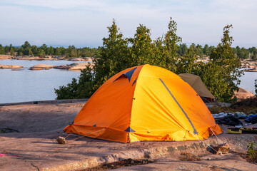 camping on georgian bay: an orange free standing two person tent pitched on granite with trees and lake huron in the background shot in fall