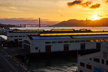 Sun setting over mountains behind Golden Gate Bridge with view from warehouses on pier