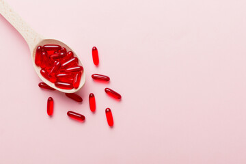 Vitamin capsules in a spoon on a colored background. Pills served as a healthy meal. Red soft gel...