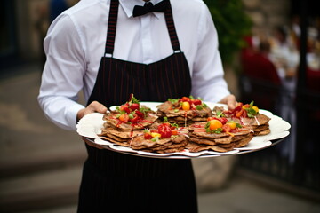 Hand of waiter from restaurant with a terrace on the beach with a view of the turquoise sea carries heavy plates with hamburgers for guests.