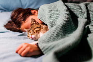 boy falls asleep and hugs his cat, who sleeps with him under the covers. children and pets. the cat sleeps with the baby. - Powered by Adobe