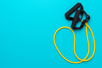 Minimalist flat lay photo of resistance band with handles over turquoise blue background. Top view...