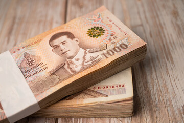 Fototapeta premium Stack of Thai baht banknotes on wooden background, business saving finance investment concept.