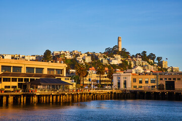 Shoreline at golden hour with docks on San Francisco Bay looking up at Telegraph Hill and Coit Tower