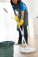 Unknown woman in maid uniform cleaning home floor with wet mop at home	