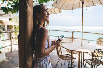 Cheerful female digital nomad using smartphone on summer terrace