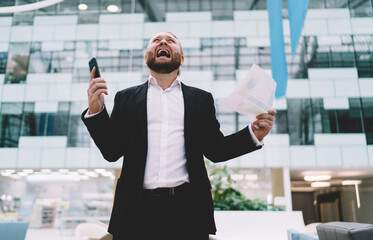 Stressed businessman screaming with smartphone and papers in hands