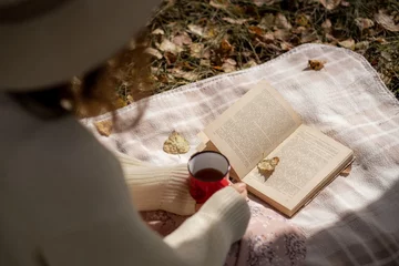 Fotobehang Chocoladebruin A young beautiful woman in a dress and a round hat reads a book outdoors in the forest and drinks tea. Romantic and vintage photo of a beautiful girl. Reading and relaxation  © Anat art