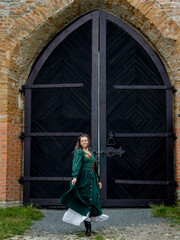 beautiful brunette woman in long green vintage dress posing in ancient castle 