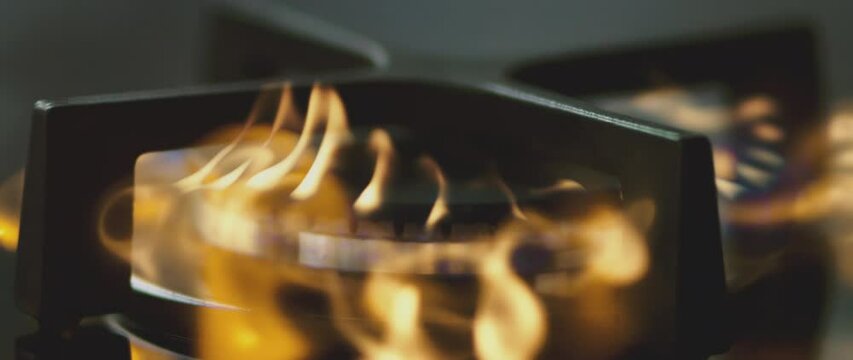 Gas stove burner ignites in extreme slow motion, with orange flames flaring before settling into a blue ring. Close-up of a kitchen hob illustrates ignition, combustion and cooking heat.