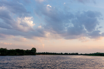 Beautiful sky over the river with fluffy blue clouds and orange sun at sunset. Dawn on the lake. Picturesque sky at sunrise