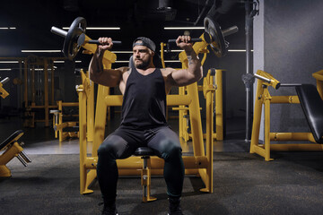 Tattooed, bearded sportsman in black sweatpants, vest and cap. He performing a chest press while...