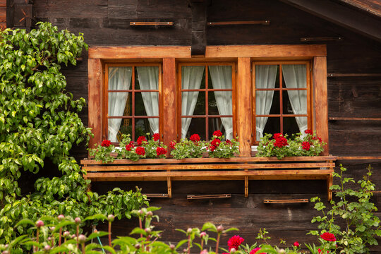 Picturesque chalet window with red geraniums in flower box in Zermatt, Switzerland, in summertime
