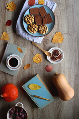 Fototapeta na wymiar Cup of tea or coffee, plate with cookies and chocolate, dried oranges, bowl of grapes, vintage books, pumpkins and autumn leaves on the table. Autumnal hygge. Top view.