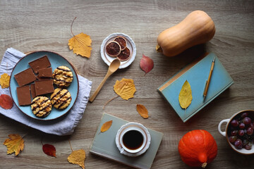 Cup of tea or coffee, plate with cookies and chocolate, dried oranges, bowl of grapes, vintage books, pumpkins and autumn leaves on the table. Autumnal hygge. Top view.