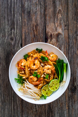 Pad Thai with prawns and rice noodles in peanut and tamarind sauce on wooden table
