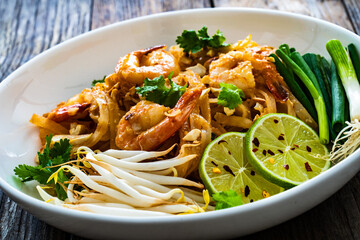 Pad Thai with prawns and rice noodles in peanut and tamarind sauce on wooden table
