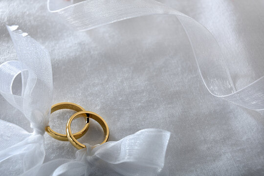 Two gold rings tied with ribbon on white cloth top