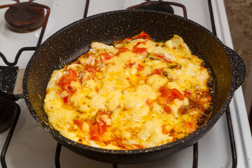 Scrambled eggs with tomatoes and sprinkled with cheese in a frying pan on the stove