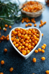 Sea buckthorn berries in a heart shaped bowl, orange healthy berries, macro. Rustic style, top view