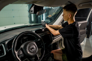 A close-up of a car wash worker using a brush and car chemicals to clean the dashboard of a luxury car during the detailing process
