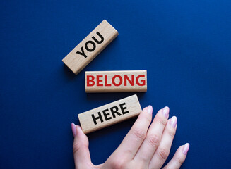 You belong here symbol. Wooden blocks with words You belong here. Beautiful deep blue background. Businessman hand. Business and You belong here concept. Copy space.