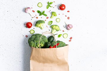 Craft paper bag with assortment of fresh organic vegetables, herbs and spices on white marble...