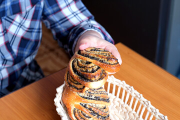 Obraz na płótnie Canvas The hands of an elderly woman operate a sweet bun with poppy seeds