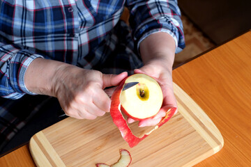 The hands of an elderly woman peel a red ripe tasty juicy apple