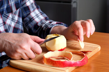 The hands of an elderly woman peel a red ripe tasty juicy apple