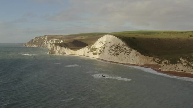 Aerial of sunlit chalk cliffs at Durdle Door, Lulworth on the Jurassic coast in Dorset with green hills behind looking out to sea, England