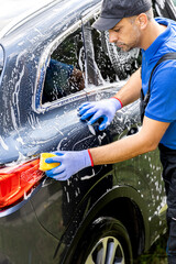 Man washing car with yellow sponge outdoors