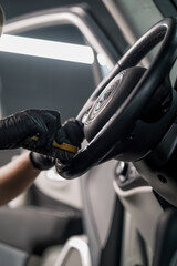 Close-up of a car wash worker cleaning the steering wheel of a luxury car with a brush and washing...