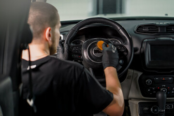 Close-up of a car wash worker cleaning the steering wheel of a luxury car with a brush and washing foam in the process of detangling