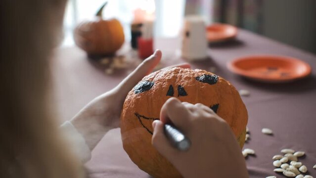 Close-up of little girl drawing scary face on pumpkin, preparing and decorating for Halloween