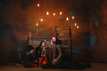 Girls in witch costumes are sitting near the fireplace making a potion, and their mother is sitting nearby.