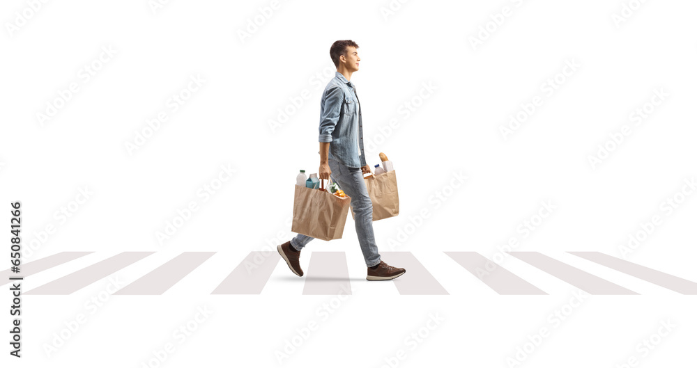 Poster full length profile shot of a male teenager carrying grocery bags over a pedestrian crossing